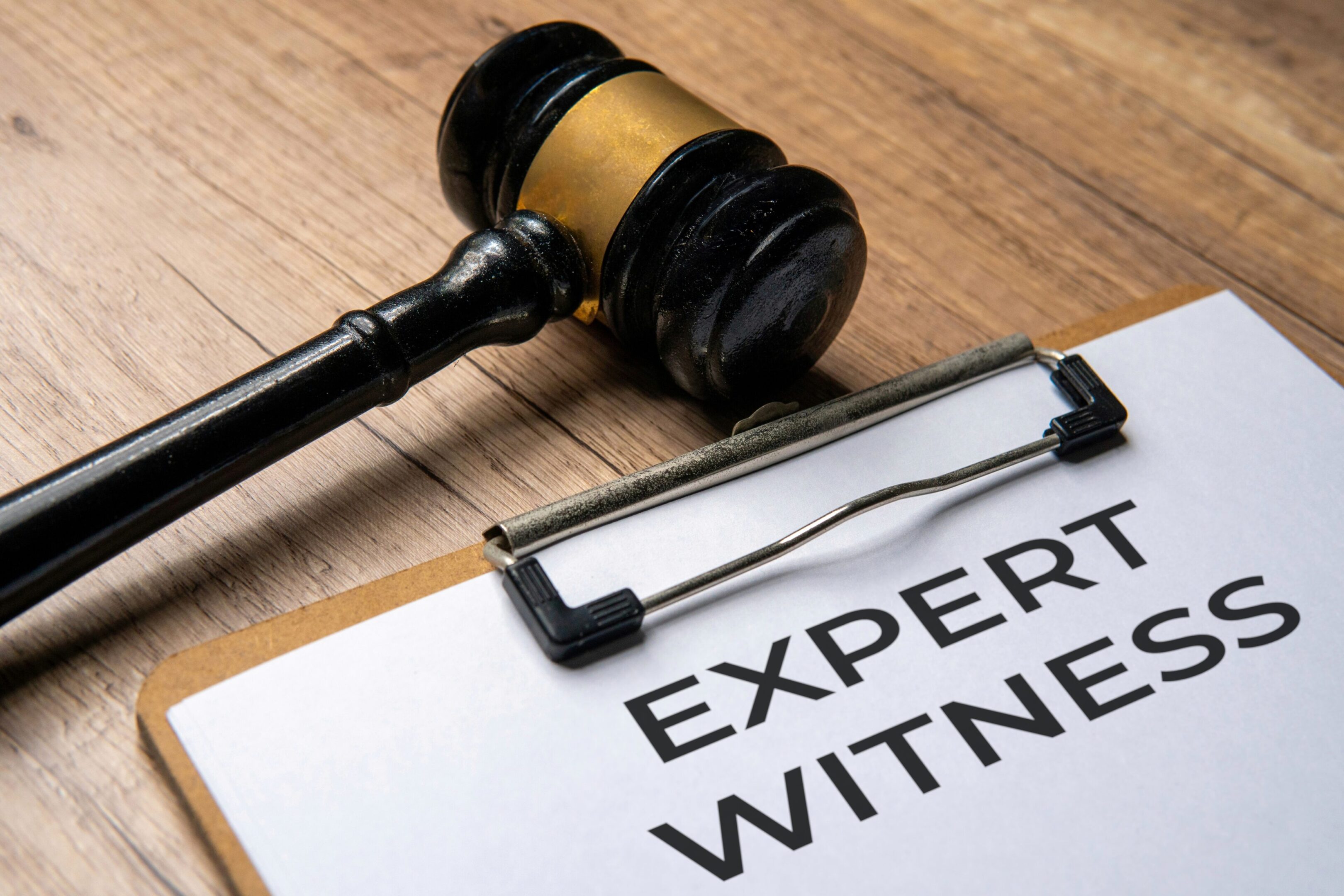 Close-up image of paper clipboard with text EXPERT WITNESS and judge gavel. Legal expertise, testimony, law concept.