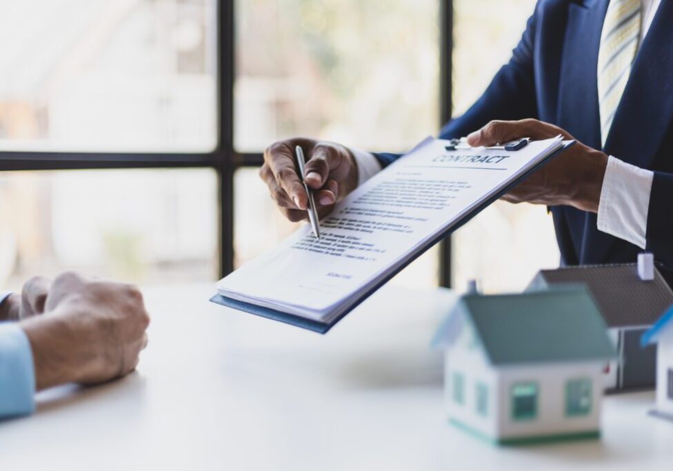 Businessman or lawyer uses pen to point at contract agreement document for client to sign.